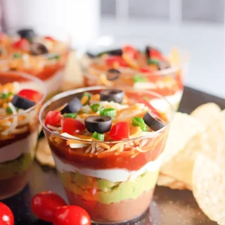 Beautiful 7 layer dip cups with colorful toppings served with tortilla chips