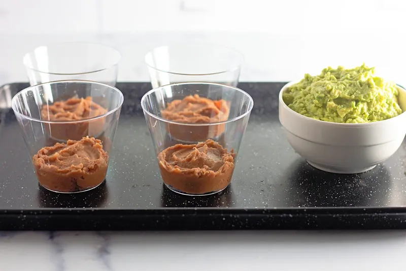 Clear cups with refried beans layer for 7 layer dip cups recipe