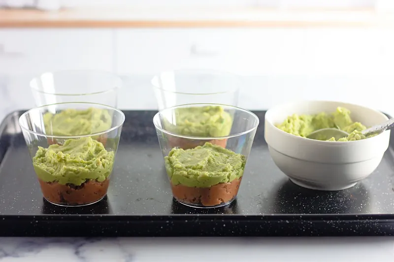 Adding guacamole layer on top of beans in clear cups