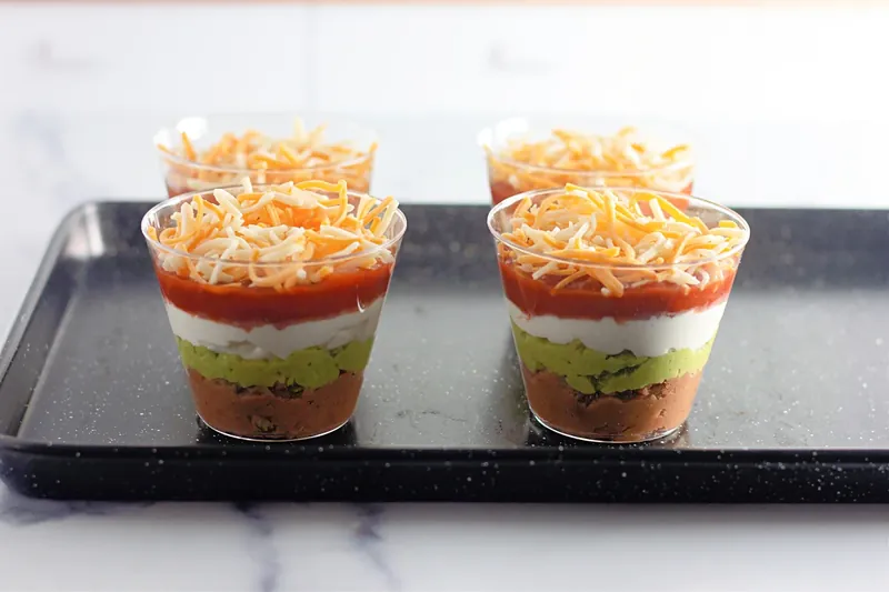 Shredded cheese being added to 7 layer dip cups