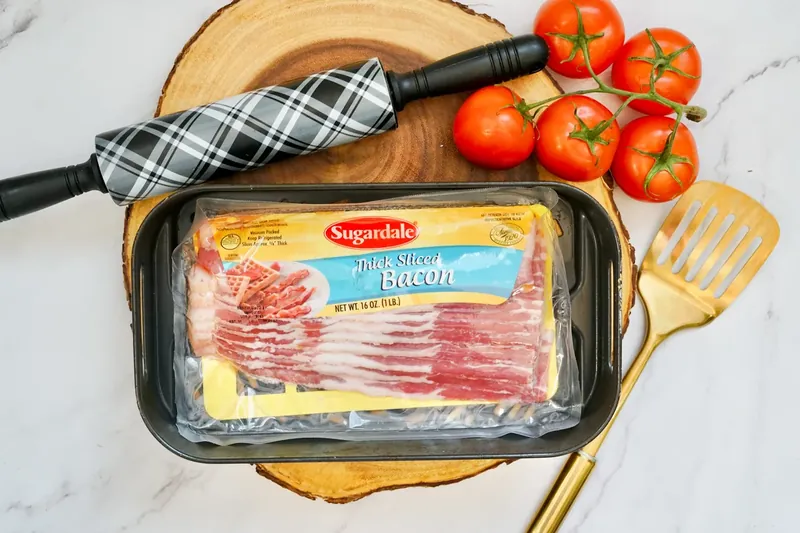 Package of thick-cut bacon on wooden board with air fryer accessories