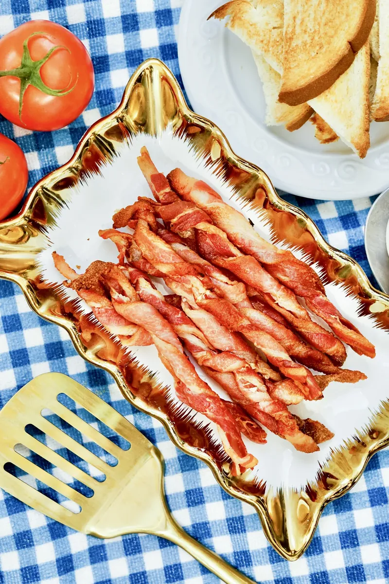Bacon twists on gold plate with toast and tomatoes on checkered cloth