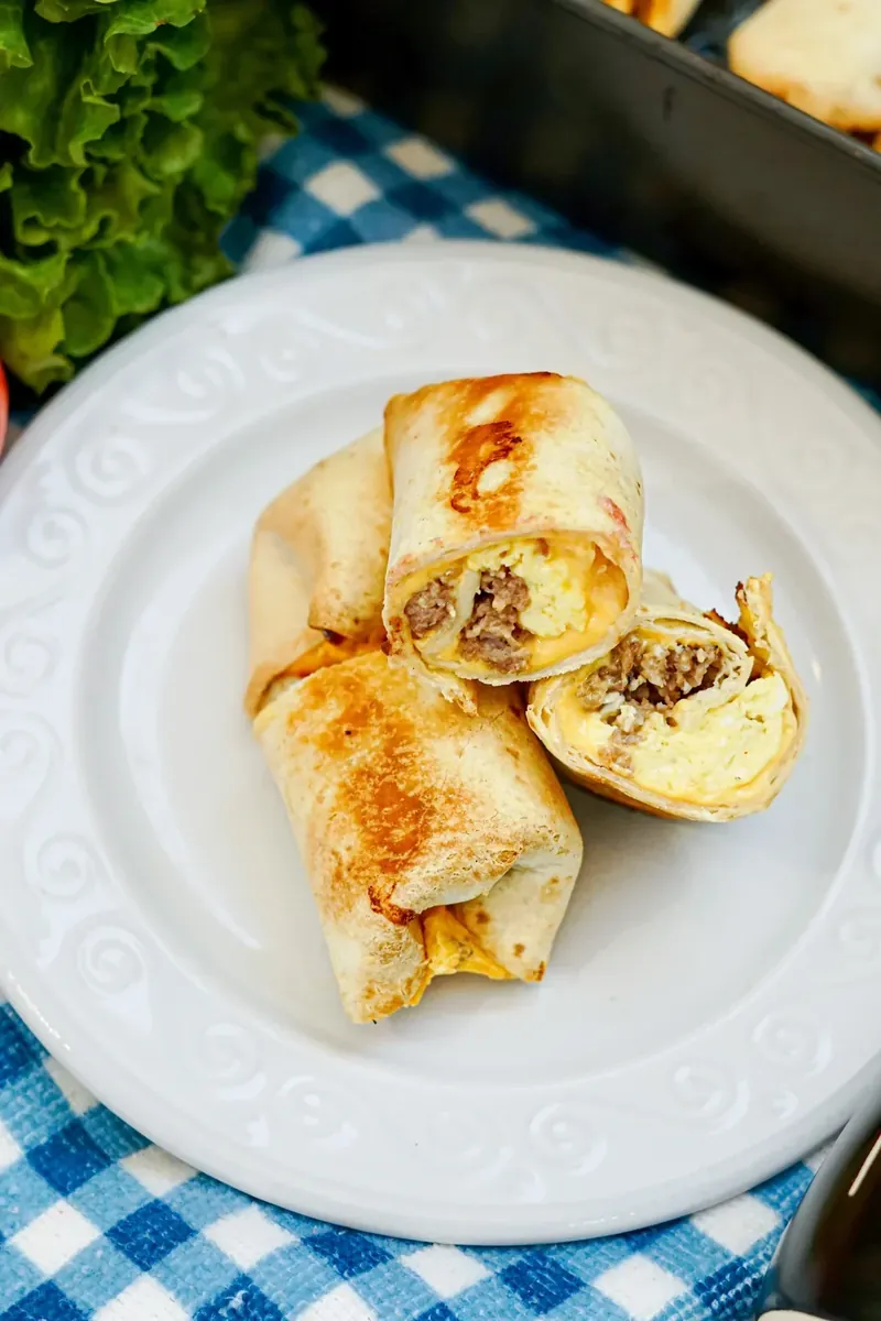 Golden brown air fryer breakfast burritos cut in half showing eggs, sausage and cheese filling