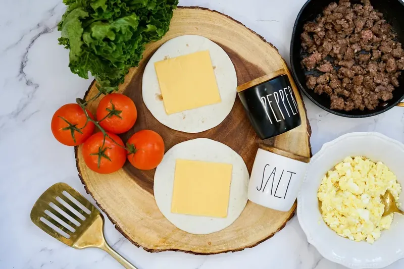Breakfast burrito ingredients including tortillas, cheese, cooked sausage, and scrambled eggs