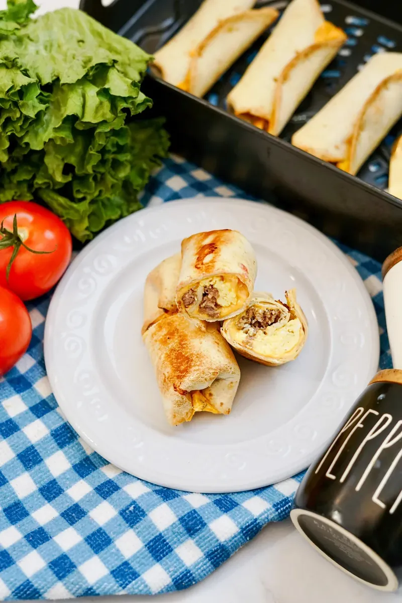 Plated air fryer breakfast burritos cut in half showing melted cheese and sausage filling