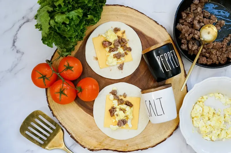 Cooked breakfast sausage being added to tortillas with eggs and cheese