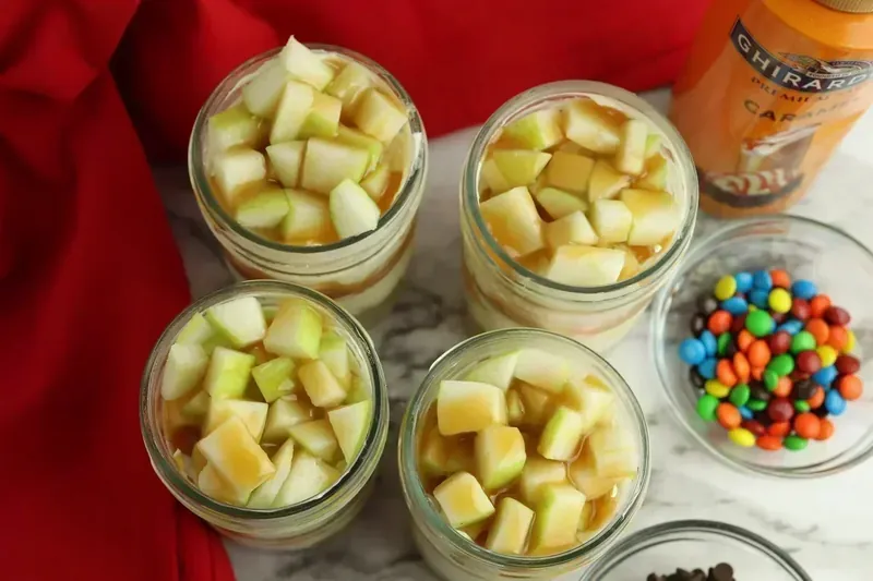 Diced green apples topped with caramel sauce drizzle on cheesecake jars