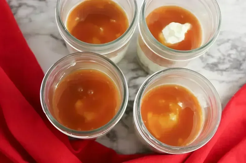 Caramel sauce being added as a middle layer in the cheesecake jars