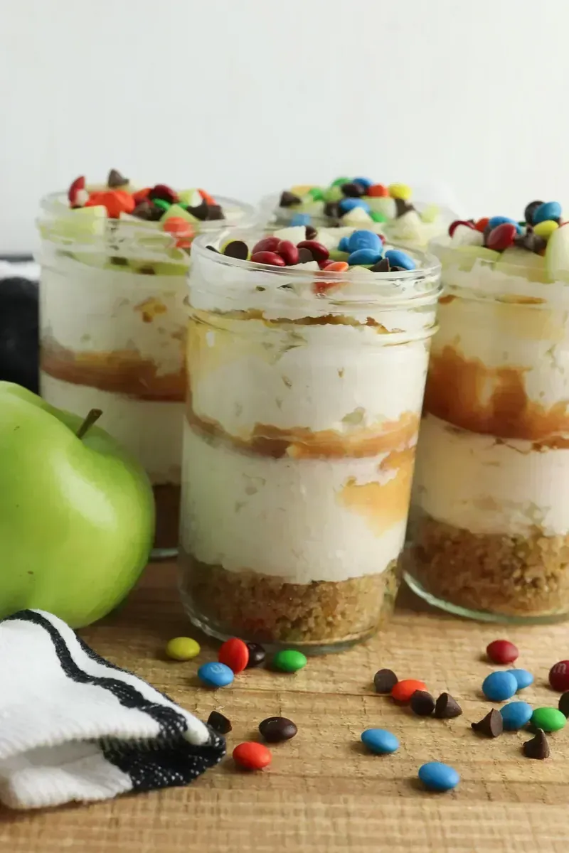 Multiple candy apple cheesecake jars showing layered presentation with caramel swirls and colorful toppings