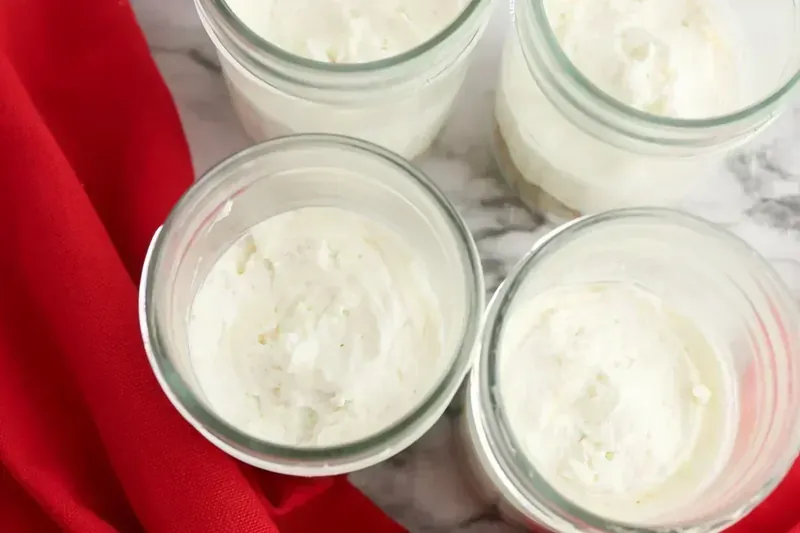Glass jars filled halfway with creamy white cheesecake mixture over graham cracker crust