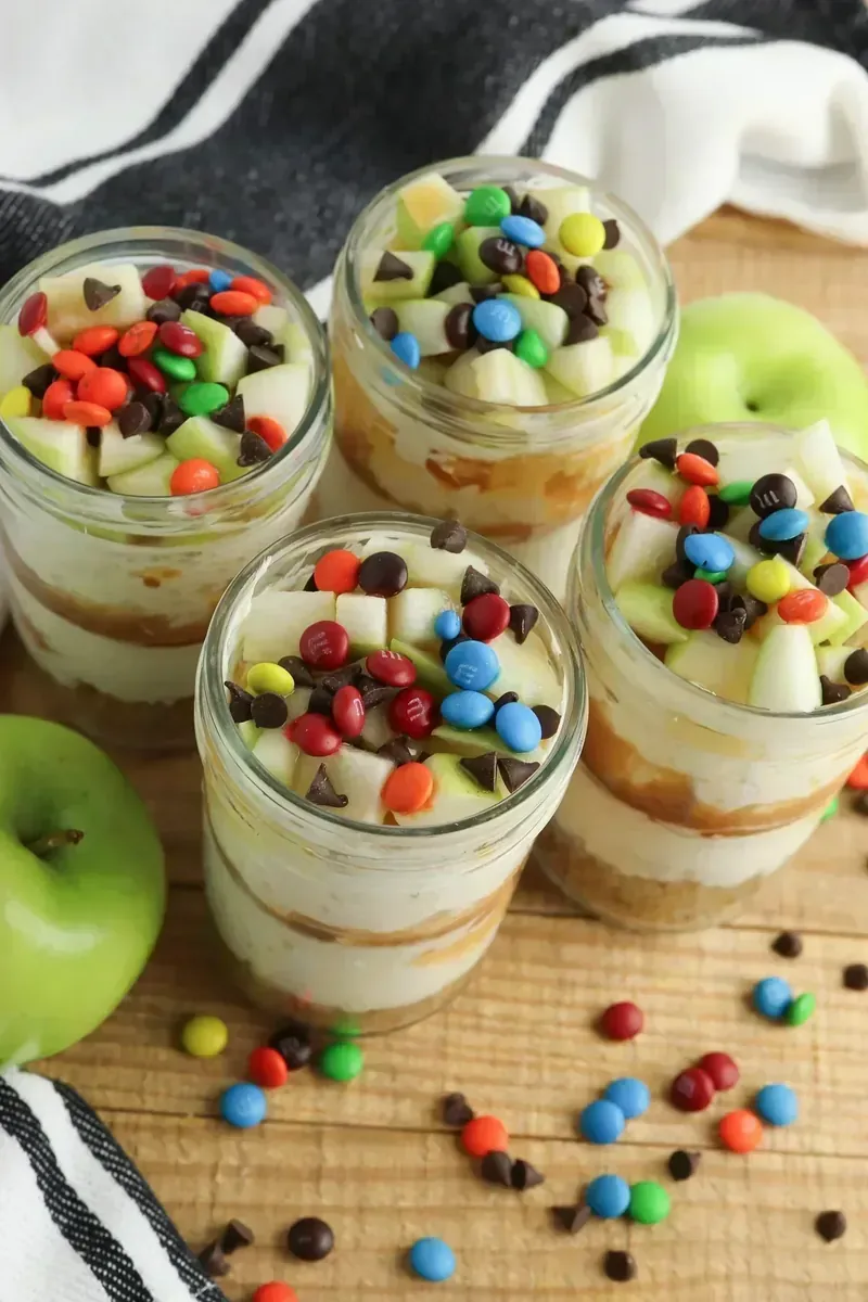 Four candy apple cheesecake jars arranged together showing consistent layering and colorful toppings
