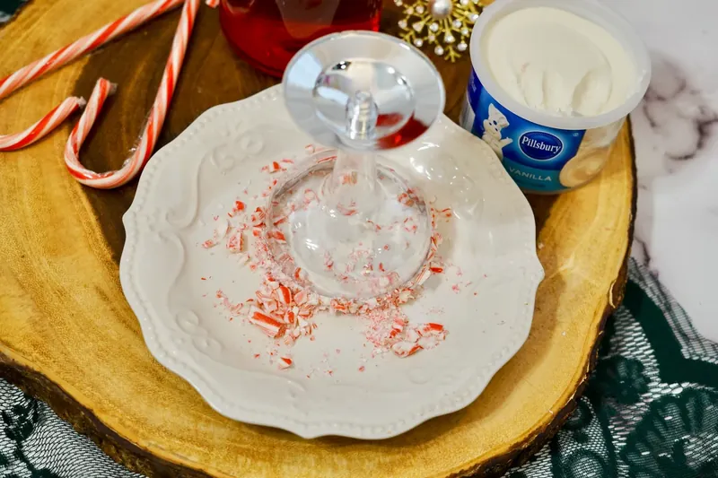 Champagne glass rim coated with vanilla frosting and crushed candy cane pieces
