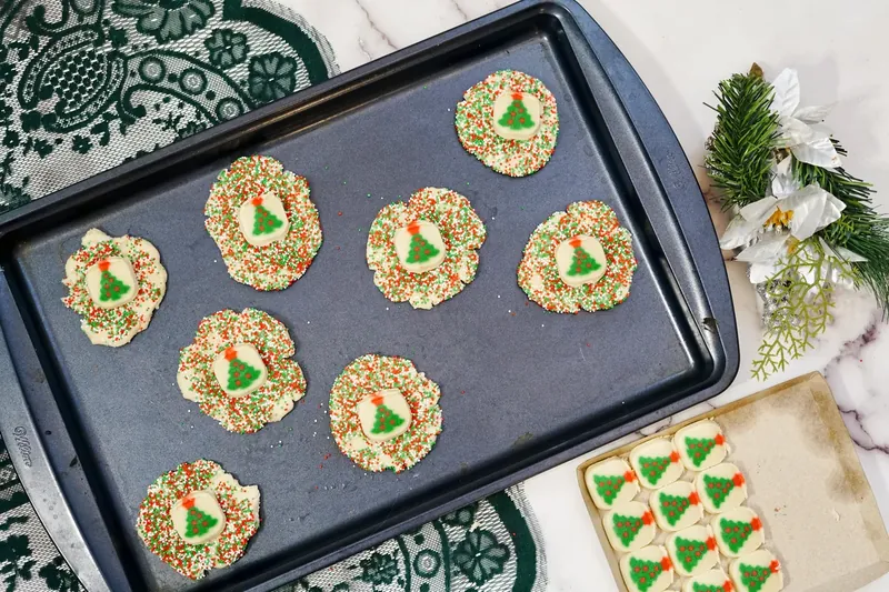 Christmas sugar cookies with tree designs placed on top of sprinkle-covered base cookies