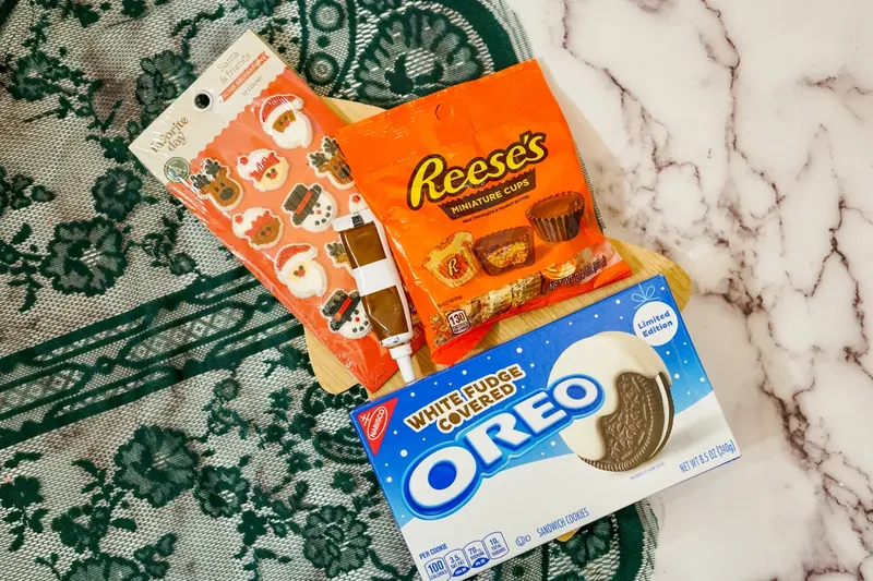 Ingredients for Christmas ornament Oreos including white Oreos, Christmas candies, mini Reese's cups and frosting