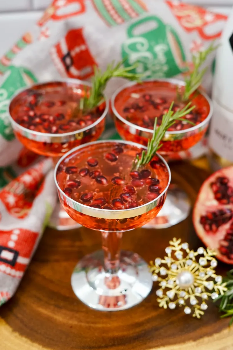Three Christmas pomegranate mimosas garnished with pomegranate seeds and rosemary sprigs