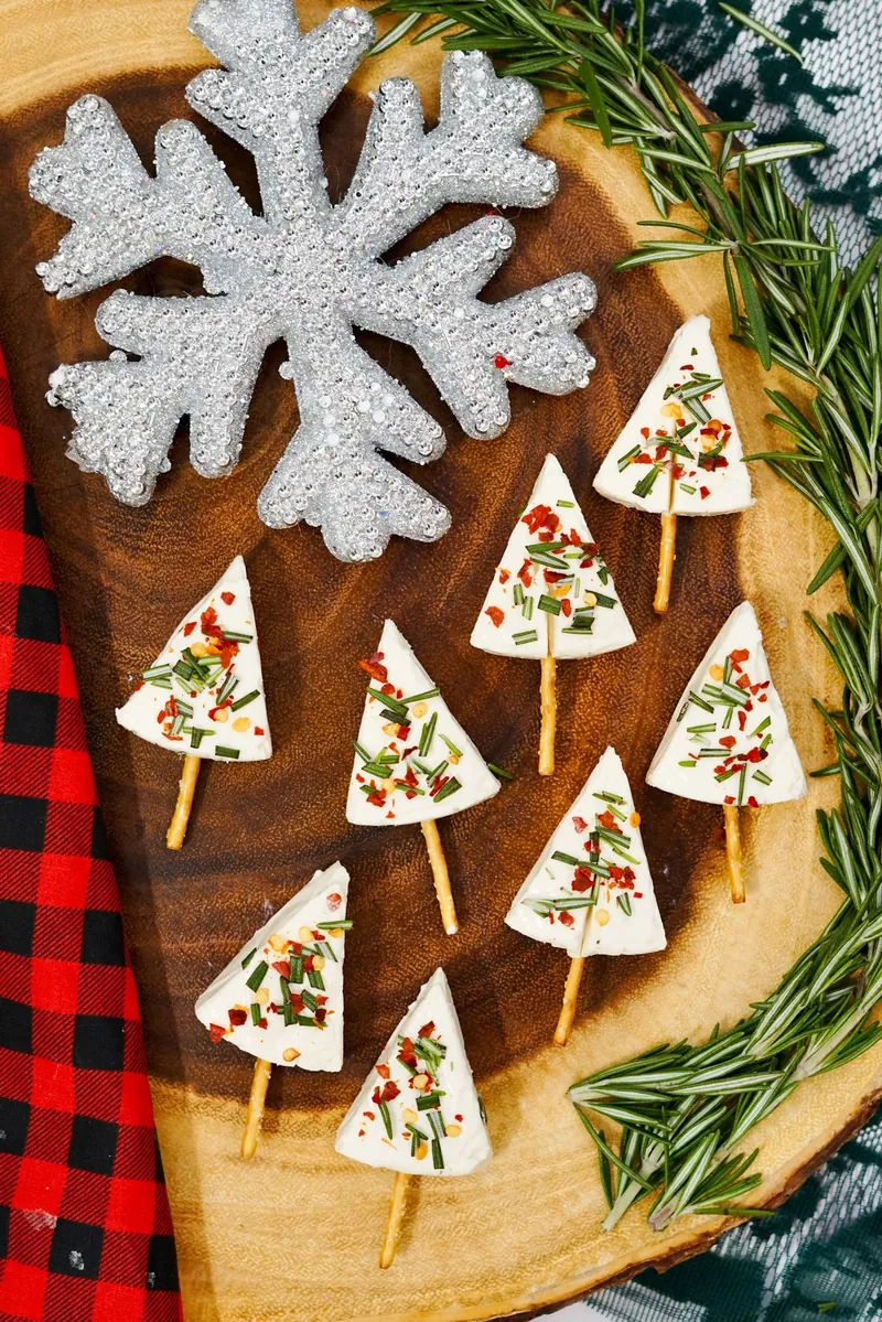 Christmas tree cheese appetizers on wooden board with snowflake decorations and plaid napkin