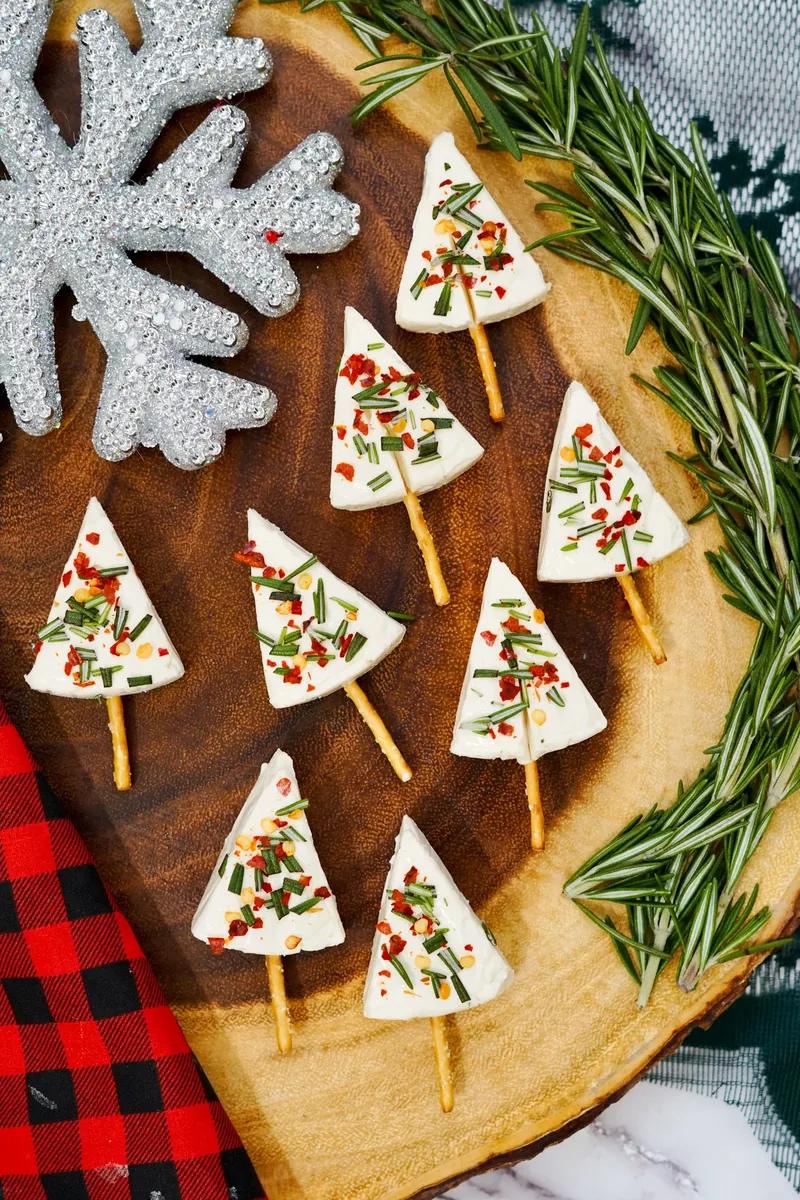Multiple Christmas tree cheese appetizers arranged on rustic wooden board with rosemary garnish