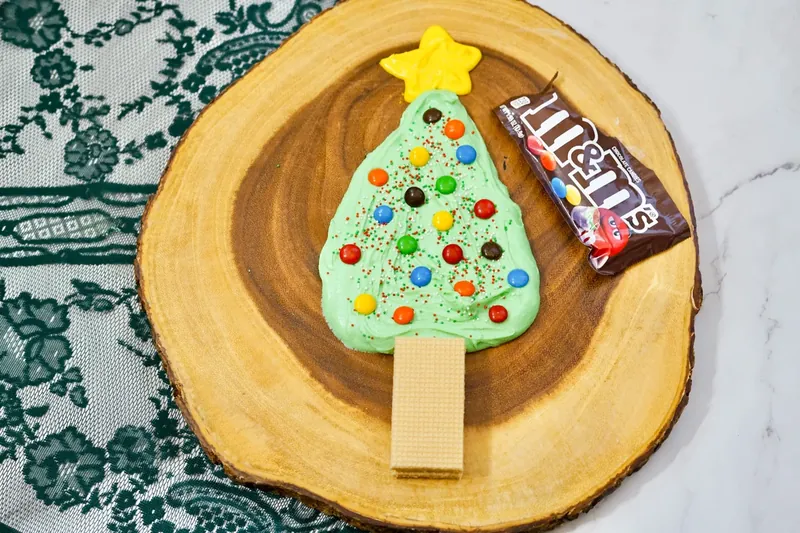 Colorful M&M candies being added as ornaments to Christmas tree frosting board