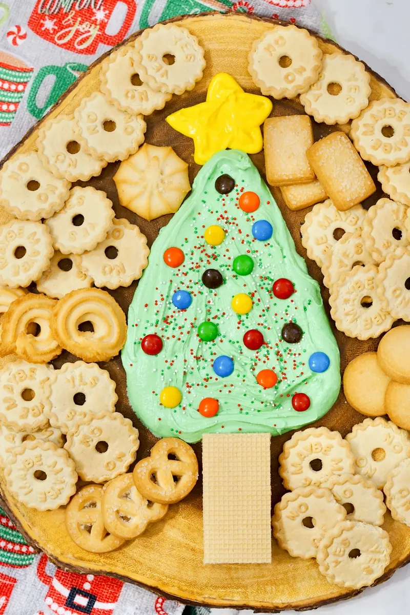 Assorted cookies arranged around completed Christmas tree frosting board for dipping
