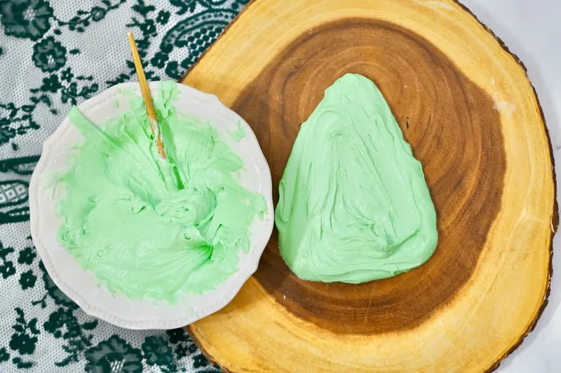 Green frosting being shaped into Christmas tree form on wooden serving board