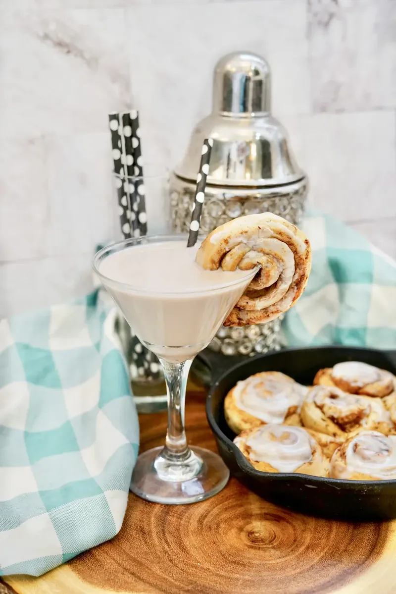 Creamy cinnamon roll martini in glass with cinnamon roll garnish and cocktail shaker