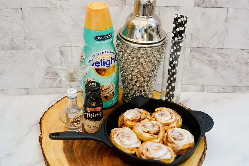 Cinnamon roll martini ingredients including Baileys, vodka, creamer, cocktail shaker and cinnamon rolls