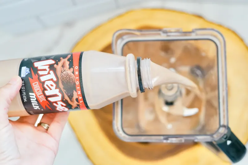 Hand pouring chocolate milk into blender for Frosty recipe