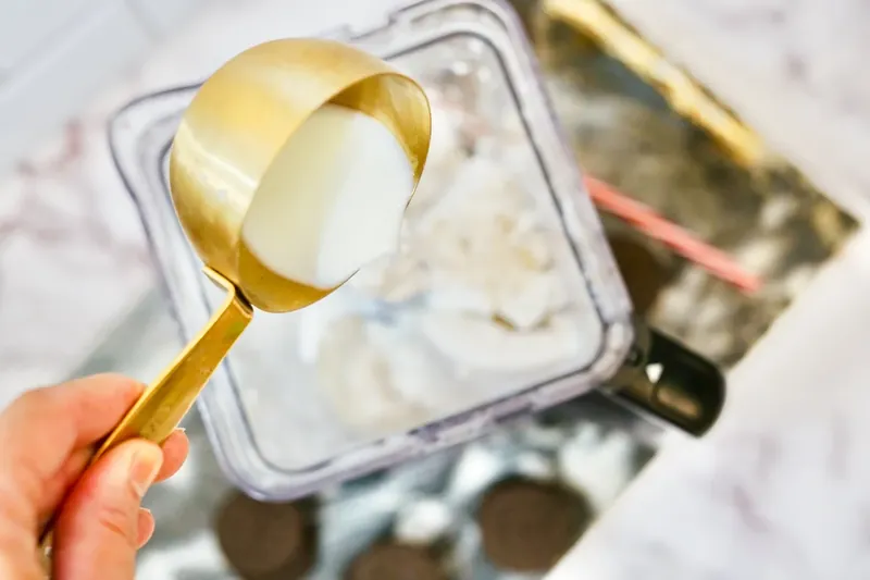 Milk being poured from measuring cup into blender with ice cream