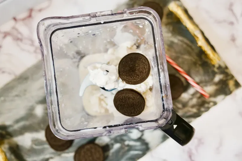 Oreo cookies being added to blender with ice cream and milk mixture