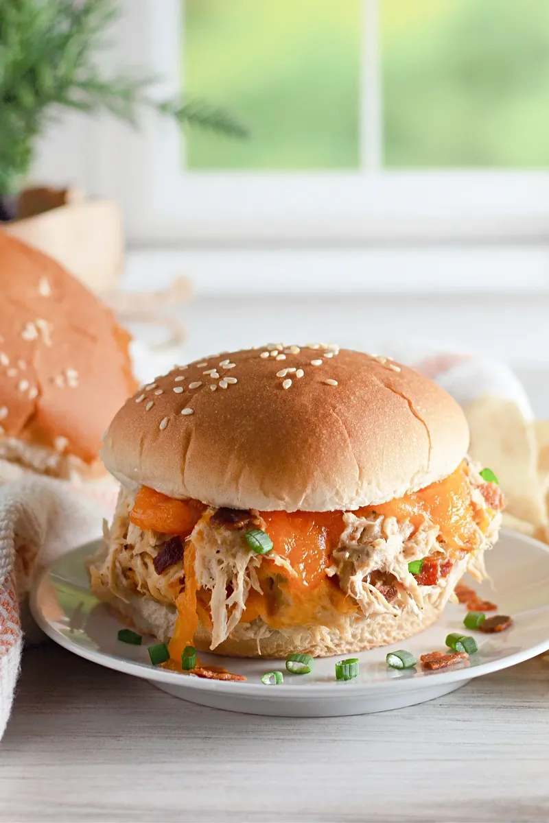 Golden crack chicken sandwich on white plate with bacon and green onion garnish