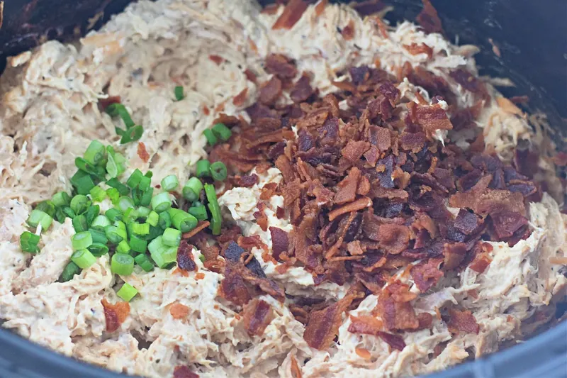 Shredded chicken mixture with crumbled bacon and chopped green onions being added