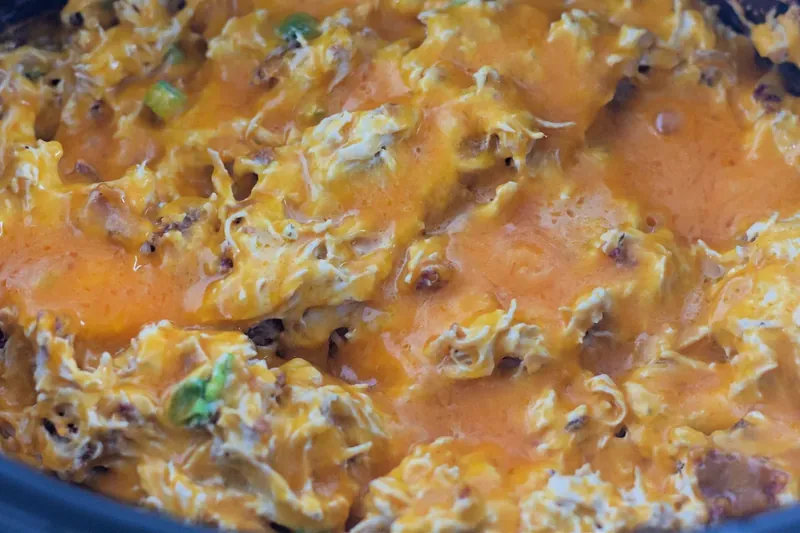 Spoon lifting creamy crack chicken mixture showing melted cheese and bacon