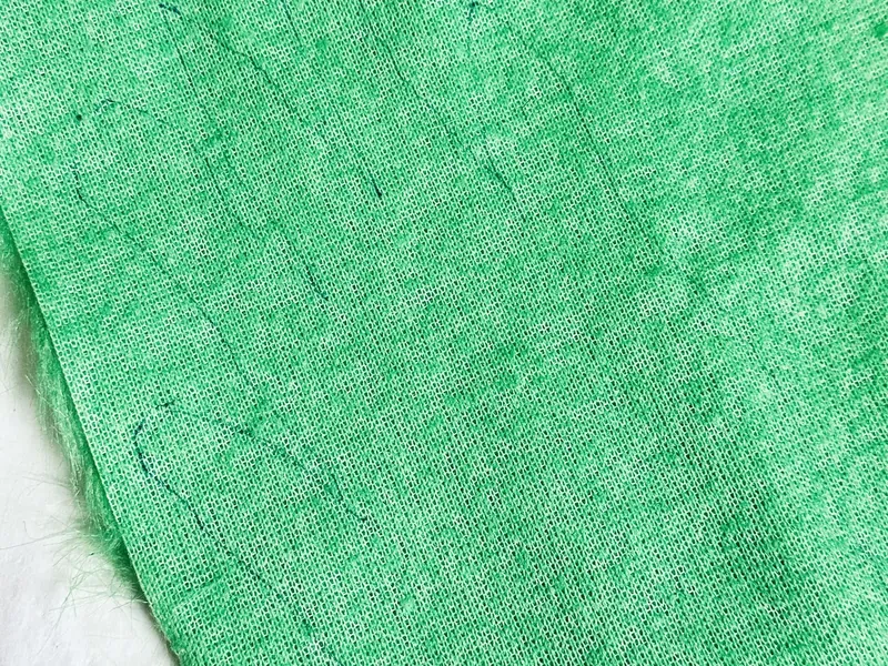 Attaching green faux fur Grinch hand to end of candy cane wreath with hot glue