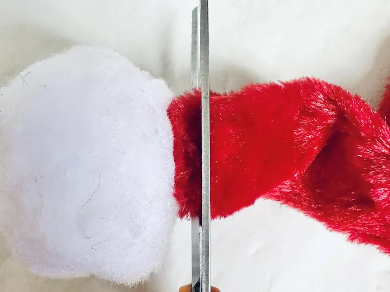 Cutting red velvet scarf with scissors to remove pom pom end for wreath project