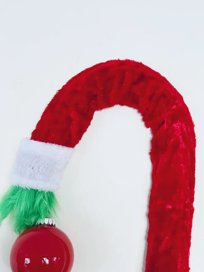 Final completed DIY Grinch wreath with red candy cane shape, white cuff, and green hand holding red ornament