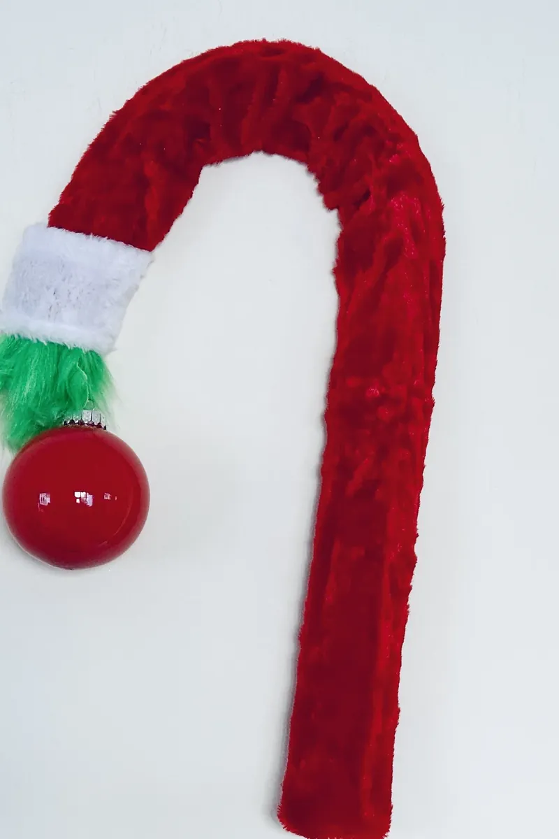 Finished Grinch wreath showing candy cane shape with red scarf, white cuff, green furry hand holding red ornament