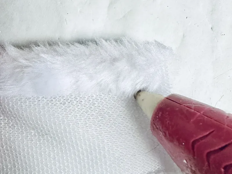 Gluing green fur fingers together around red ornament string to secure ornament to Grinch hand