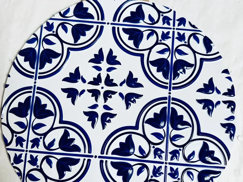 Blue and white decorative tile being attached to Dollar Tree ornament base with hot glue