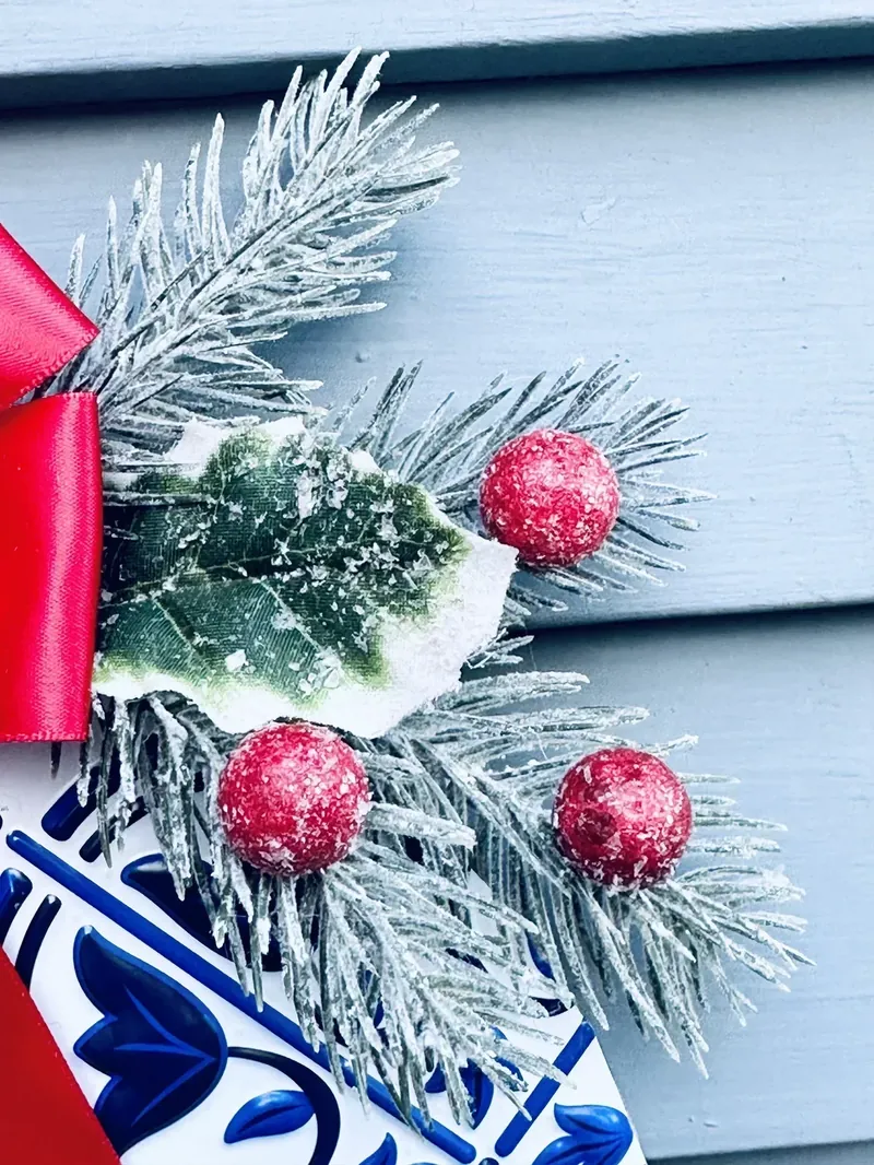 Close-up detail of ornament wreath showing red holly berries, frosted pine branches, and decorative elements
