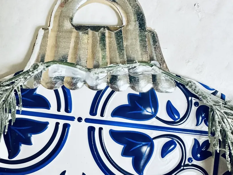 Metal ornament cap being reattached to top of tile-covered ornament with pine greenery