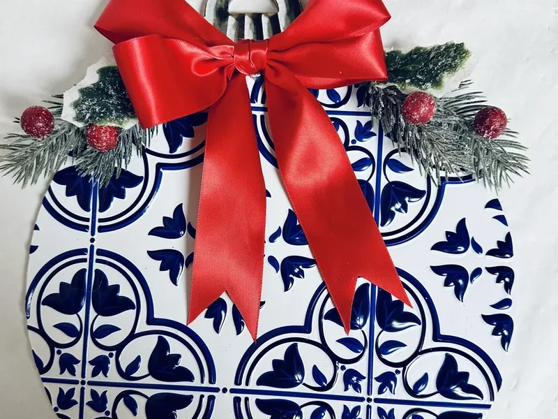 Red satin ribbon bow being attached to center of ornament wreath covering pine stems