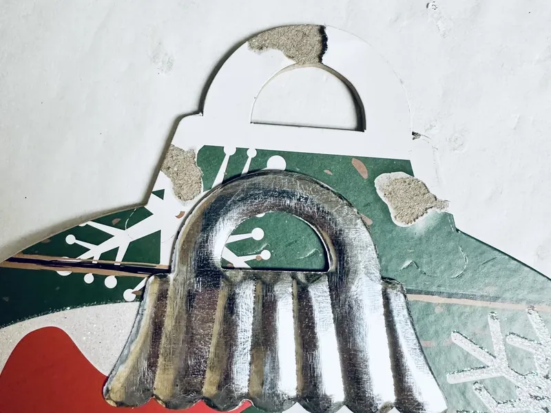 Hands removing metal ornament cap from Dollar Tree round sign for wreath craft project