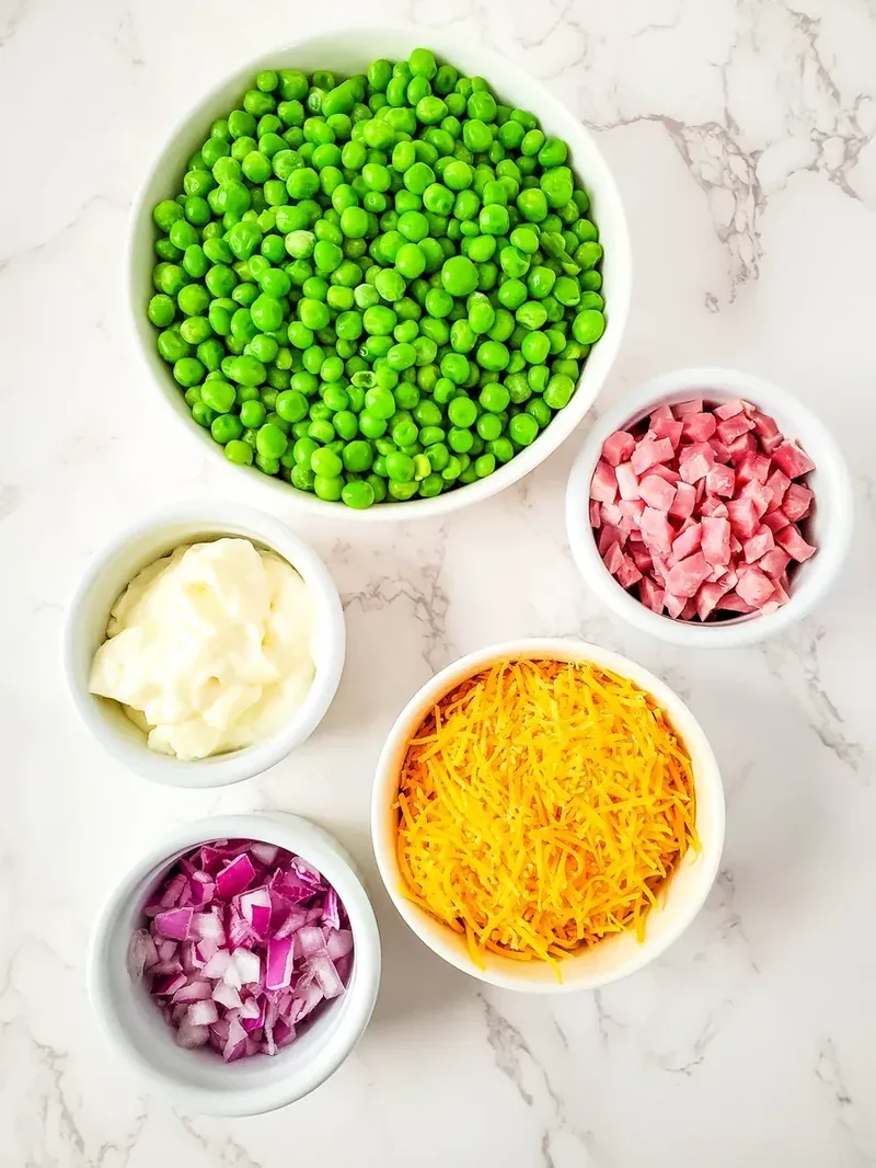 Individual ingredients for ham and pea salad in white bowls