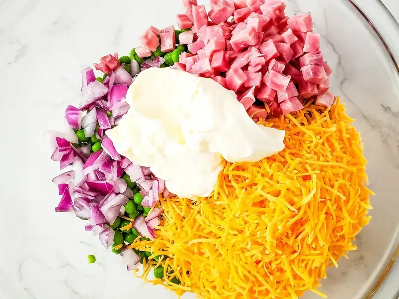 Mayonnaise being added to ham and pea salad ingredients