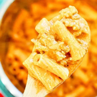 Close-up of creamy sausage rigatoni on wooden spoon showing texture