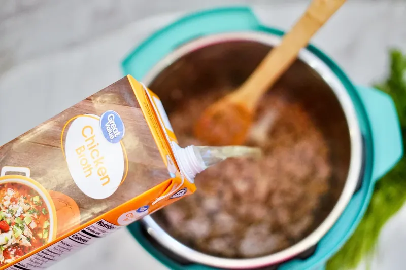 Chicken broth being poured into Instant Pot with cooked sausage