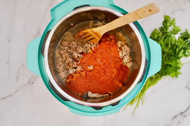 Tomato pasta sauce being added to Instant Pot with sausage and broth