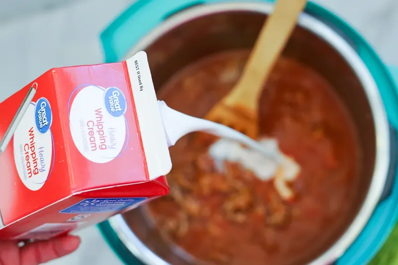Heavy cream being poured into Instant Pot pasta mixture