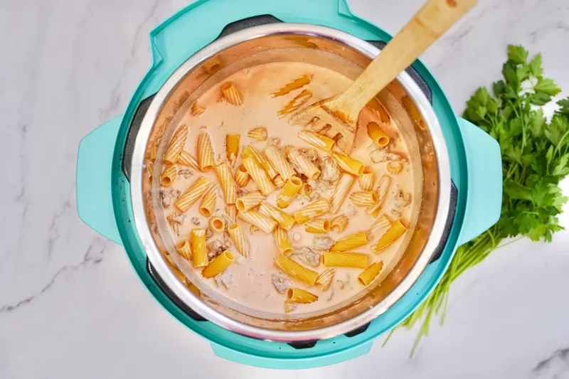 Rigatoni pasta being added to creamy sauce mixture in Instant Pot