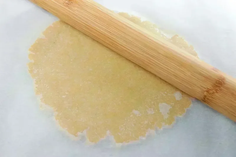 Rolling keto pastry dough with rolling pin between parchment paper